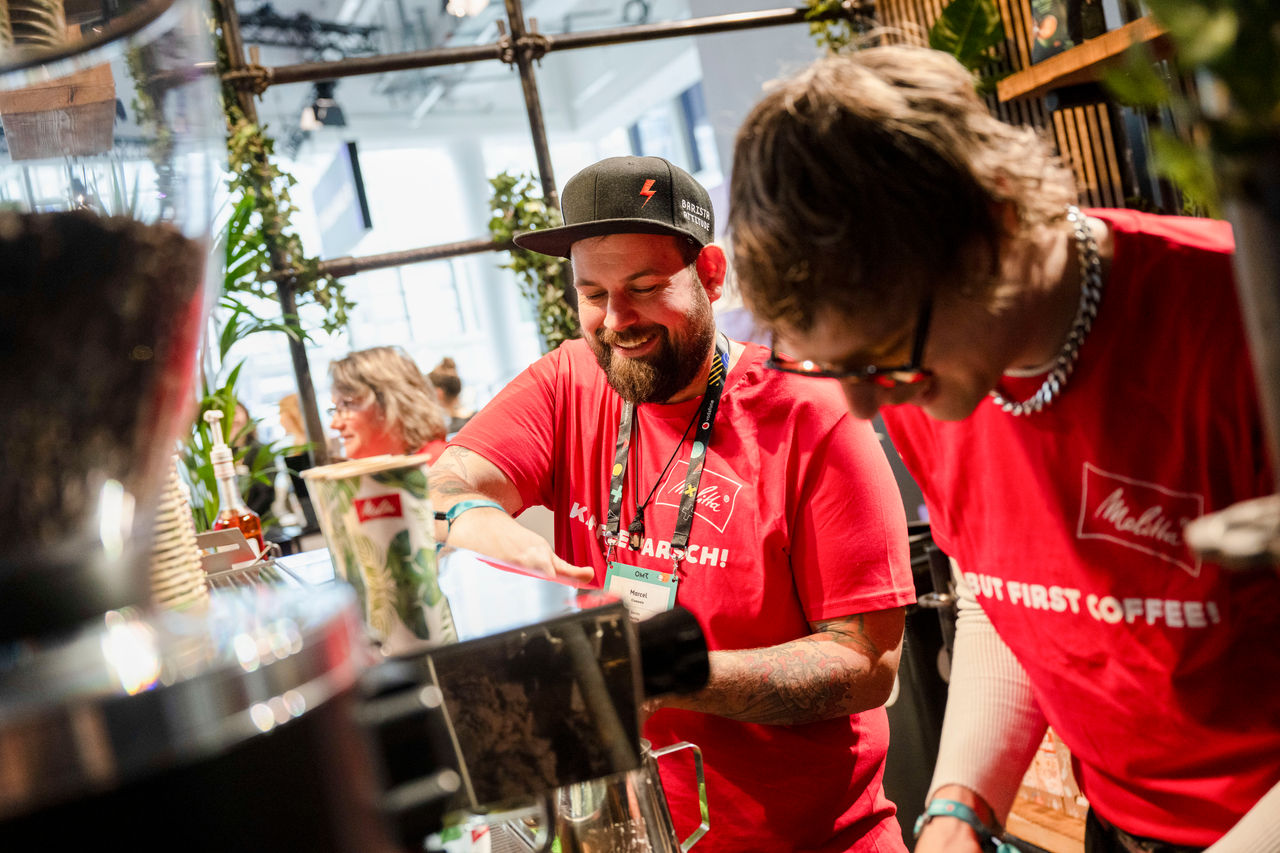 Baristi in roten Melitta Shirts machen Kaffee