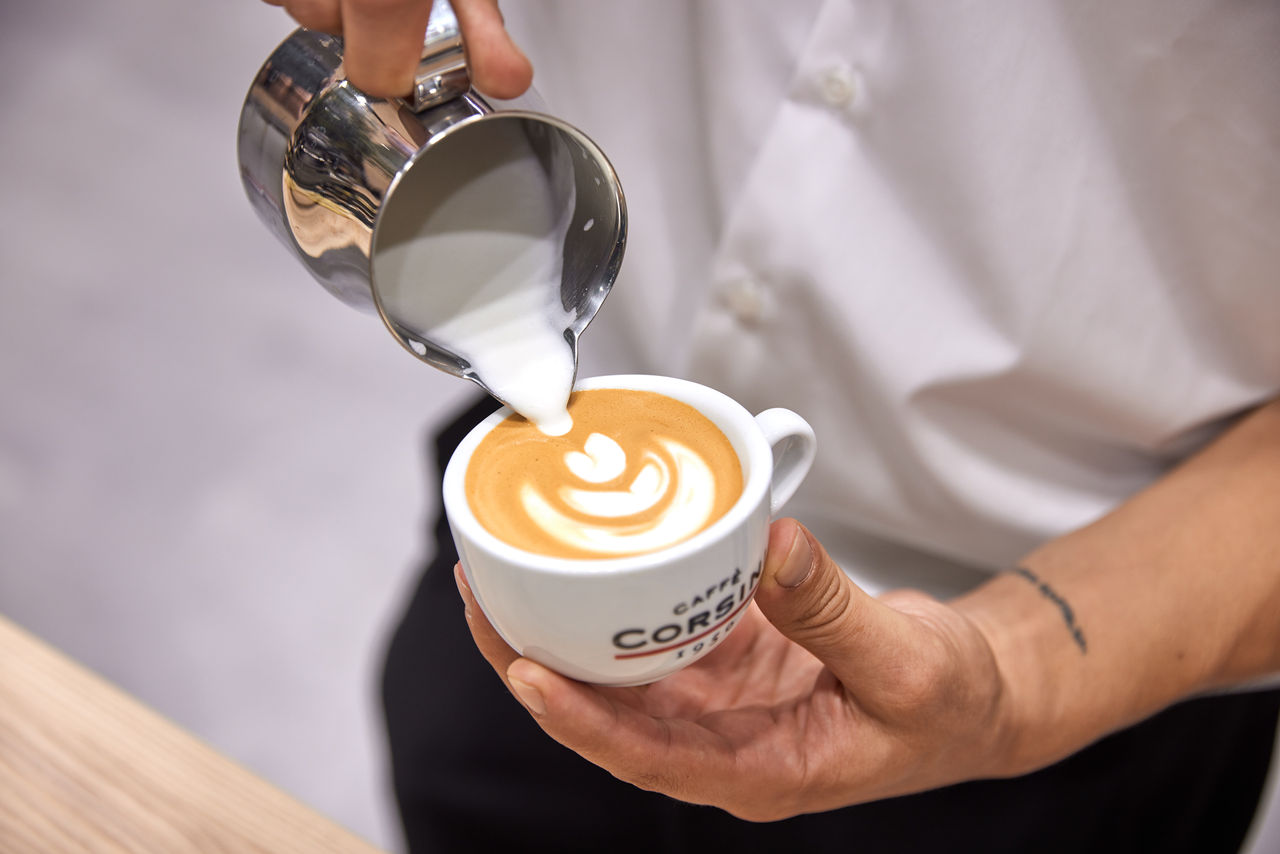 Detailaufnahme wie Barista Kaffeekunst in einer Caffè Corsini Tasse bereitet 